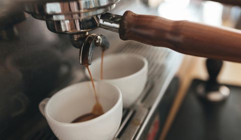 Coffee machine making coffee and pouring into white cups in coffee shop