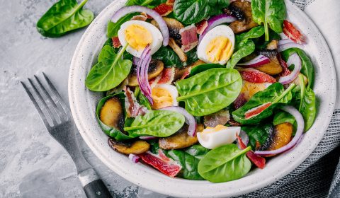 lunch bowl of spinach salad with bacon, mushrooms, eggs and red