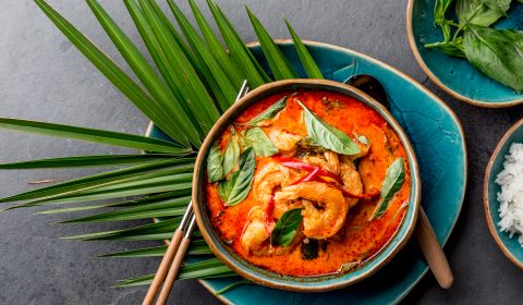 THAI SHRIMPS RED CURRY. Thailand Thai tradition red curry soup with shrimps prawns and coconut milk. Panaeng Curry in blue plate on gray background