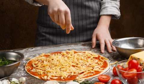 Preparing pizza. Woman adding cheese to pizza